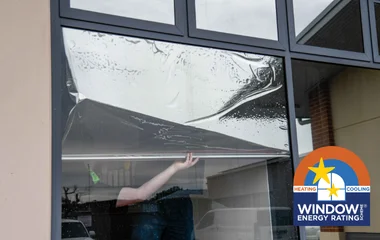 A close-up of reflective silver film being applied to a large commercial window, featuring the official WERS (Window Energy Rating Scheme) logo in the corner to highlight energy efficiency compliance.