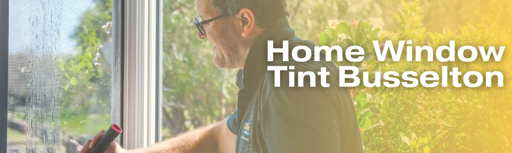 Banner image for South West Windscreens & Tint with bold white text overlay reading 'Home Window Tint Busselton' alongside a technician in a branded polo shirt applying window tint film to a residential window with a warm sunlit garden visible in the background.
