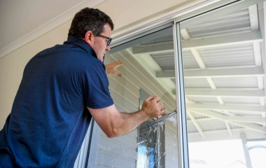 South West Windscreens & Tint technician applying window tint film to a large sliding glass door inside a residential property in Busselton, Western Australia.