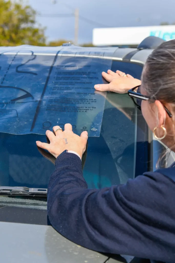 Melissa Armstrong, co-owner of South West Windscreens & Tint in Busselton, holding a windscreen chip assessment guide against a vehicle windscreen to evaluate the size and location of stone chip damage.