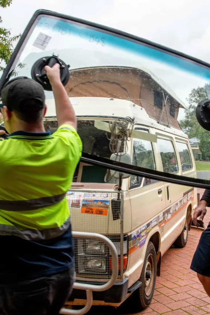 South West Windscreens & Tint technician in a hi-vis shirt using a suction cup tool to lift and position a large replacement windscreen on a 4WD vehicle during an on-site glass replacement.